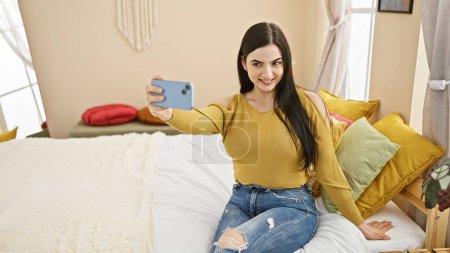 Photo for Attractive young hispanic woman taking a selfie in a stylish bedroom setting. - Royalty Free Image