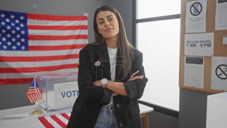 Selbstbewusste junge hispanische Frau mit verschränkten Armen steht in einem amerikanischen Wahllokal, das mit der Flagge der Vereinigten Staaten geschmückt ist.