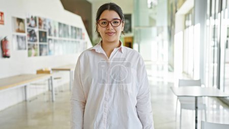 Téléchargez les photos : Portrait d'une jeune femme hispanique dans un bureau portant des lunettes et une chemise blanche, respirant la confiance et le professionnalisme. - en image libre de droit
