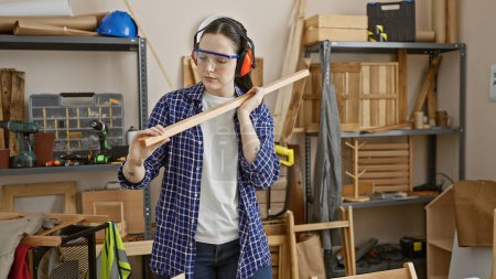 A young woman examines lumber in a well-equipped carpentry workshop, showcasing creativity and craftsmanship.
