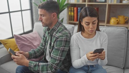 A man and woman sit apart on a sofa engrossed in their phones, highlighting modern indoor disconnection.