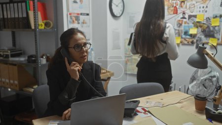 Photo for Two women investigators work diligently in an office, one on the phone, amidst evidence and clues for a case. - Royalty Free Image