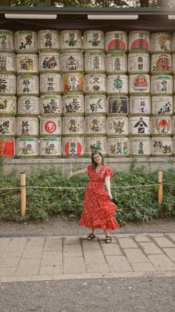 Hermosa mujer hispana sonriendo, de pie por barriles batidos en el templo meiji mientras abraza la cultura japonesa, todo mientras se pone gafas