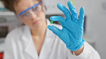 Photo for A young hispanic woman with curly hair examines a capsule in a laboratory setting, wearing protective gloves and eyewear. - Royalty Free Image