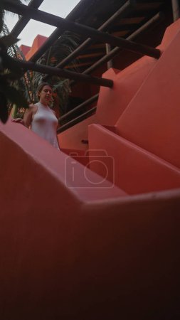 Téléchargez les photos : Une jeune femme hispanique descend des escaliers extérieurs dans un complexe bali, incarnant beauté et tranquillité. - en image libre de droit