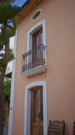 Mediterranes Haus mit Balkon, pfirsichfarbenen Wänden und Holztür, das eine ruhige europäische Atmosphäre heraufbeschwört.