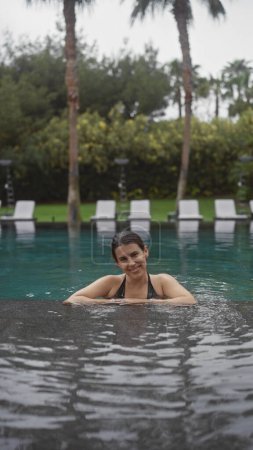 Foto de Una hermosa mujer morena se relaja en una piscina al aire libre bali resort, encarnando el ocio y la serenidad tropical. - Imagen libre de derechos