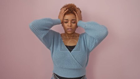 Photo for A stressed african american woman with hands on head against a pink background, portraying worry or headache. - Royalty Free Image