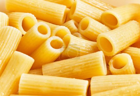 Close-up of cooked penne pasta with a glistening texture against a warm background.