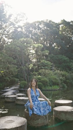 Hermosa mujer hispana sentada en un camino de piedra, disfrutando del verde esplendor veraniego de la naturaleza junto a un sereno lago en heian jingu, kyoto - un viaje divino, mirando alrededor del templo tradicional japonés