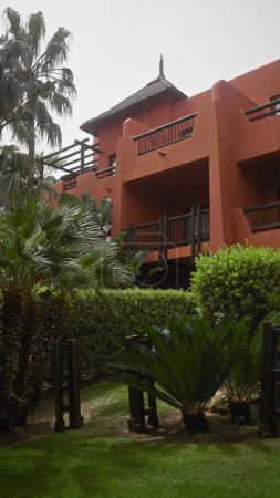 Téléchargez les photos : Station tropicale avec bâtiment en terre cuite, jardins luxuriants, palmiers et toit de chaume traditionnel. - en image libre de droit