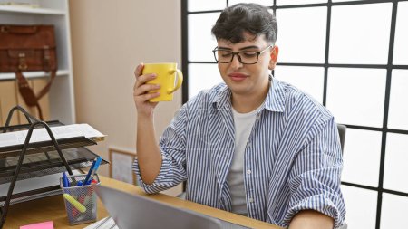 Ein junger Mann mit Gläsern hält eine Kaffeetasse in der Hand, während er eine Pause in einem modernen Büroambiente einlegt, das an lässige Professionalität erinnert..