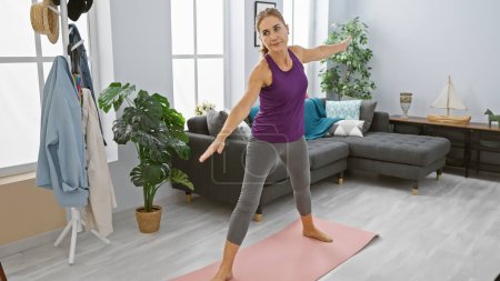 Téléchargez les photos : Femme mûre pratiquant le yoga dans un salon spacieux et bien éclairé, incarnant la santé et la tranquillité. - en image libre de droit