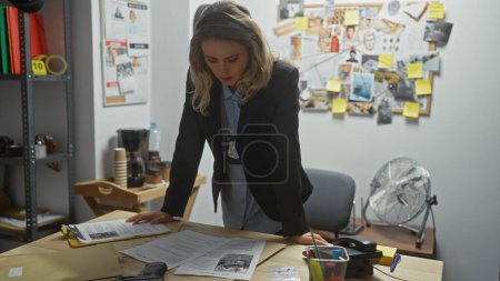 Photo for A young woman detective analyzes documents in a cluttered police station office. - Royalty Free Image