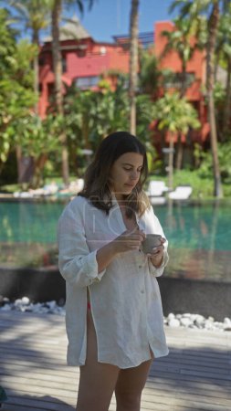 Foto de Una mujer joven disfruta de una mañana tranquila con café en un lujoso bali resort, que incorpora relajación y elegancia tropical. - Imagen libre de derechos