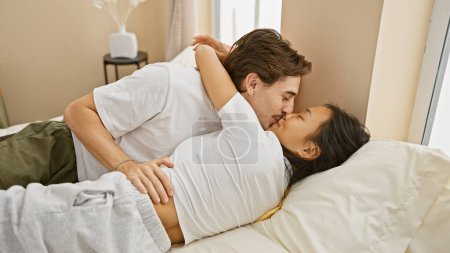 Interracial couple in love sharing an intimate moment in a cozy bedroom, with a woman and man embracing each other.