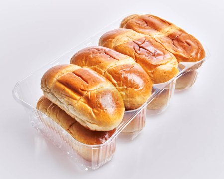 Shiny golden brioche buns in a clear plastic container on a white background convey freshness and convenience.