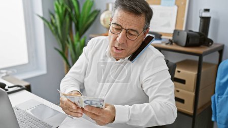 Téléchargez les photos : Mature businessman in office multitasking with phone and counting singapore dollars - en image libre de droit