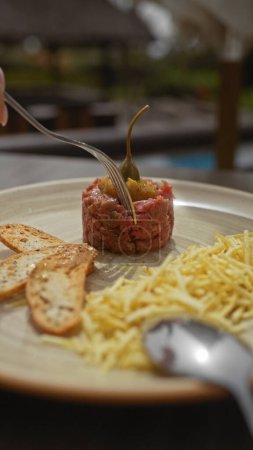 Photo for A close-up of a gourmet steak tartare adorned with a caper, served alongside toast and shredded cheese, on a ceramic plate. - Royalty Free Image