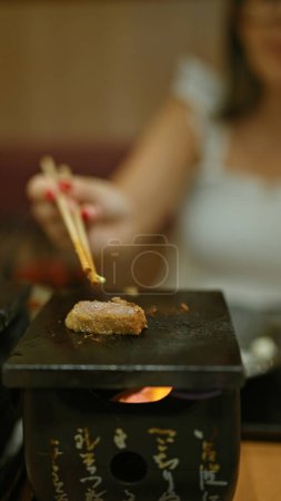 Foto de Deliciosa cena, joven mujer saboreando el tradicional gyukatsu japonés en un restaurante moderno, comida hecha a mano con plato de carne asada, usando sus prácticos palillos para el crujiente, katsu cocinado. - Imagen libre de derechos