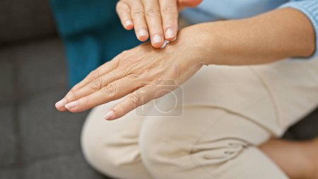 Photo for A hispanic woman applies cream to her hands at home, signaling self-care and wellness in an indoor setting. - Royalty Free Image