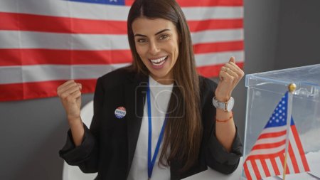 Young hispanic woman celebrating voting in indoor american electoral center with usa flag