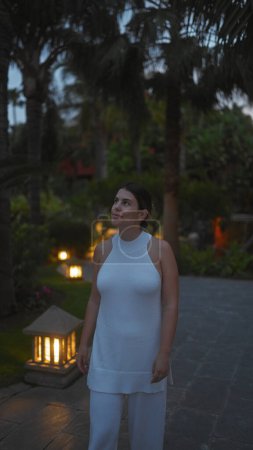 Téléchargez les photos : Une jeune femme hispanique vêtue de blanc pose à l'extérieur dans une station bali crépusculaire, respirant tranquillité et élégance. - en image libre de droit