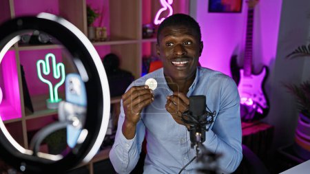 An african american man showcases a bitcoin in a modern, vibrant gaming room at night.