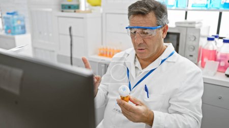 Téléchargez les photos : Homme mûr en blouse de laboratoire examine le flacon de médecine dans un laboratoire hospitalier lumineux - en image libre de droit