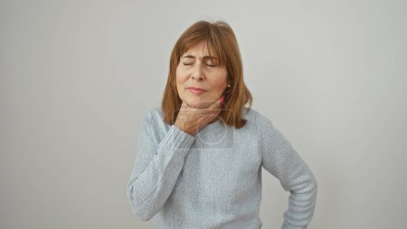 Mujer madura en malestar sosteniendo su garganta contra un fondo blanco expresando dolor