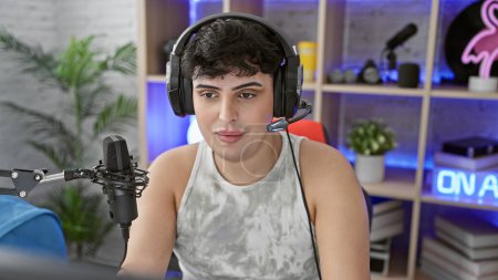Un joven en una sala de juegos con auriculares, micrófono y un letrero 'en el aire', que transmite transmisión en línea o podcasting.