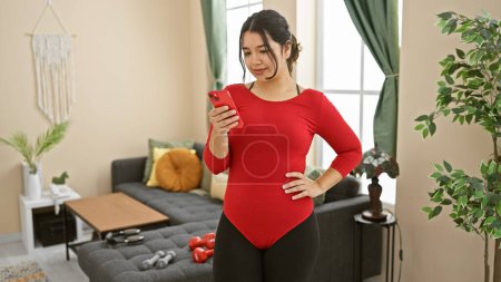 Eine attraktive hispanische Frau in Sportbekleidung checkt zu Hause ihr Handy und deutet ein Fitness- oder Technologiethema an.