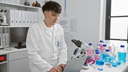 Un joven con una bata de laboratorio analizando datos de una computadora portátil en un laboratorio moderno con equipo científico