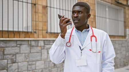 Téléchargez les photos : Un médecin noir parlant sur un smartphone à l'extérieur d'un hôpital en milieu urbain. - en image libre de droit
