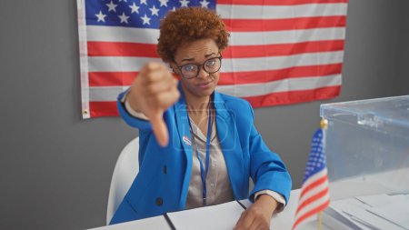 Foto de Mujer afroamericana dando pulgares abajo en un centro de votación con nuestra bandera. - Imagen libre de derechos