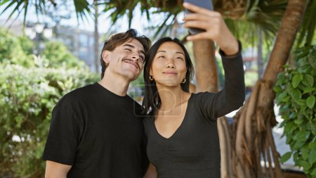 Interracial couple takes a selfie outdoors surrounded by greenery, showcasing love and connection in a natural setting.