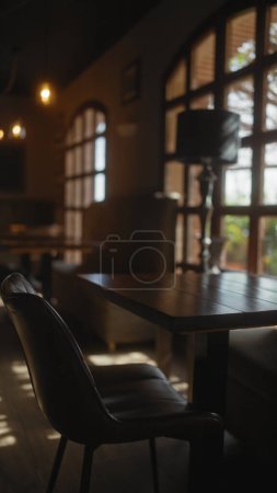Foto de Moody interior de un café débilmente iluminado con una silla vacía y mesa de madera, invocando una sensación de soledad y reflexión. - Imagen libre de derechos