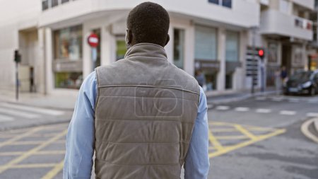 Photo for Rear view of an african american man standing at a city crosswalk, exuding urban vibes. - Royalty Free Image
