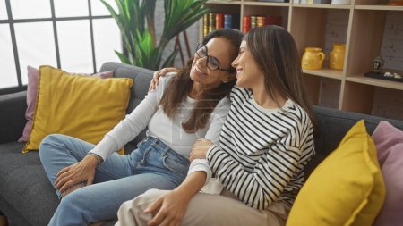 Woman and her adult daughter sharing a tender moment on a cozy couch in a stylish living room.