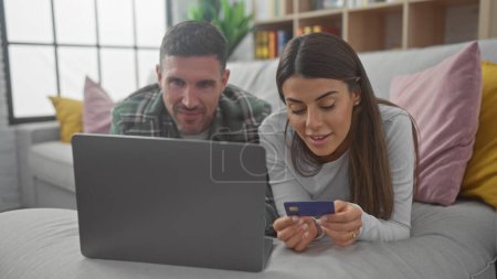 Couple shopping online together on a laptop in their cozy living room with the woman holding a credit card