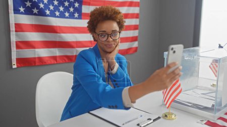 Une femme afro-américaine prend un selfie dans un centre de vote d'un collège électoral américain, avec des drapeaux.