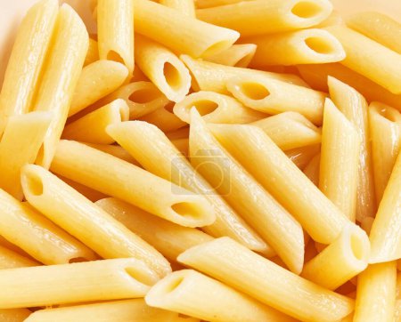 Close-up view of cooked penne pasta with a yellow color indicative of an italian dish.
