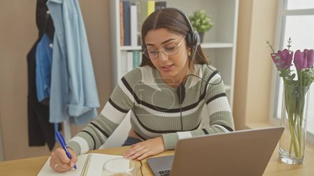Photo for A young woman with headphones working on a laptop at home, showcasing a modern freelance or remote work lifestyle. - Royalty Free Image