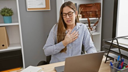Photo for A young woman experiences chest pain while working at her office, indicating potential health issues in a workplace setting. - Royalty Free Image