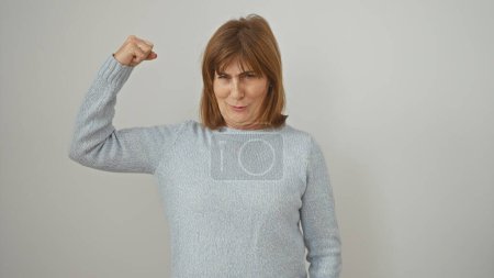 Foto de Mujer de mediana edad confiada flexionando su músculo del brazo contra un fondo blanco, mostrando fuerza y positividad. - Imagen libre de derechos