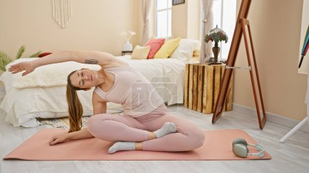 Foto de Una mujer en forma se estira sobre una esterilla de yoga en una habitación acogedora, creando una escena de bienestar serena. - Imagen libre de derechos