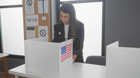 Eine junge hispanische Frau wählt in einem Raum des amerikanischen Wahlkollegs mit einer Fahne