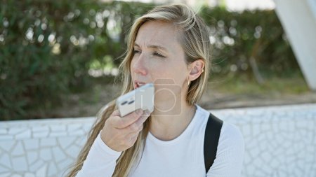Blonde woman audio messaging on smartphone in park