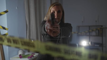 Foto de Una mujer seria detective apuntando un arma en una sala de la escena del crimen con cinta de precaución y evidencia. - Imagen libre de derechos