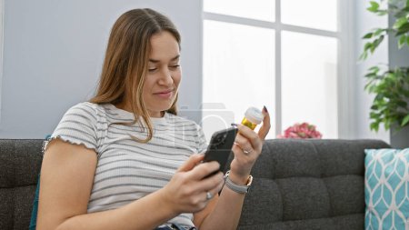 Téléchargez les photos : Une femme concentrée examine la médecine assis sur un canapé avec un téléphone dans un salon confortable. - en image libre de droit